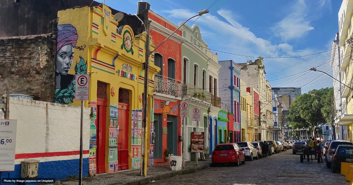 Rua colorida de casario histórico no centro do Recife, com fachadas pintadas, mural de arte urbana e carros estacionados